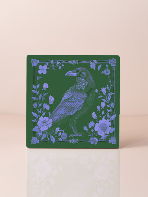 Square ceramic coaster featuring intricate lavender illustration of a raven surrounded by botanical elements on forest green background, with ornate border design and cork backing.